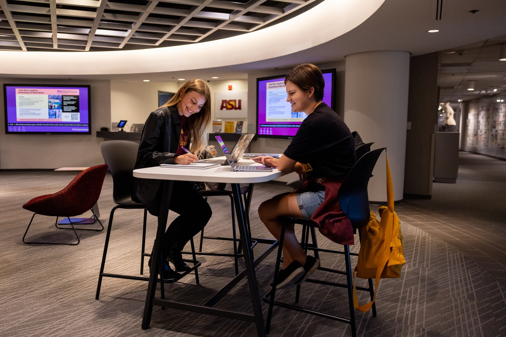 Two students sitting together in a workspace on campus.